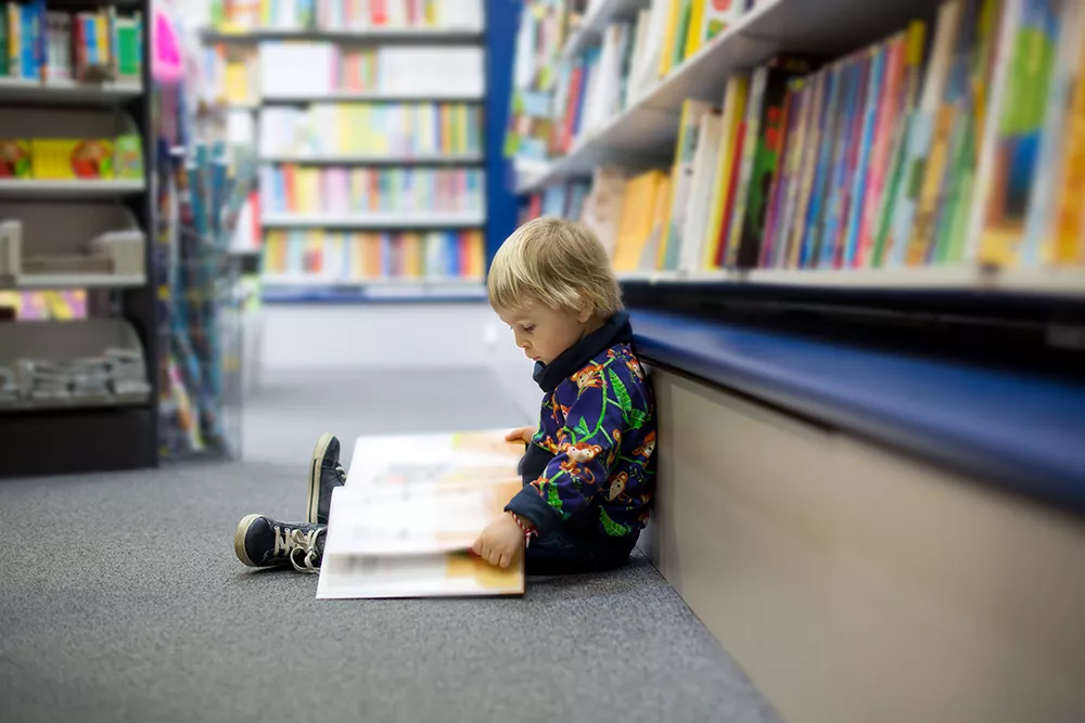 Little boy, sitting in a library and reading book