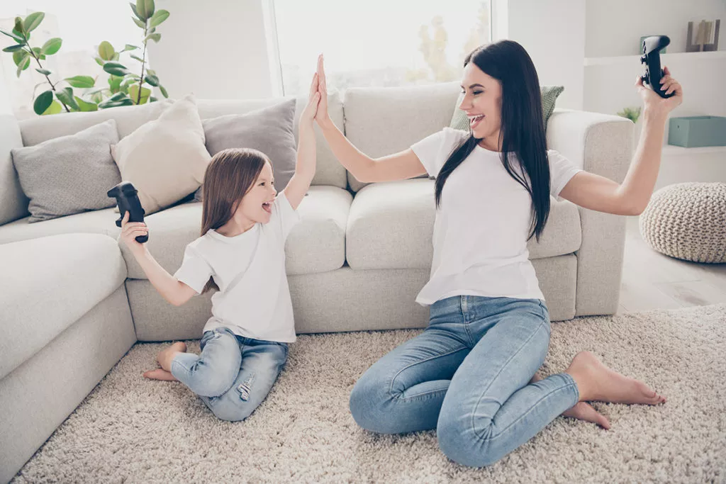 Mother and daughter giving each other a hi five on the floor by the couch as they play video games.